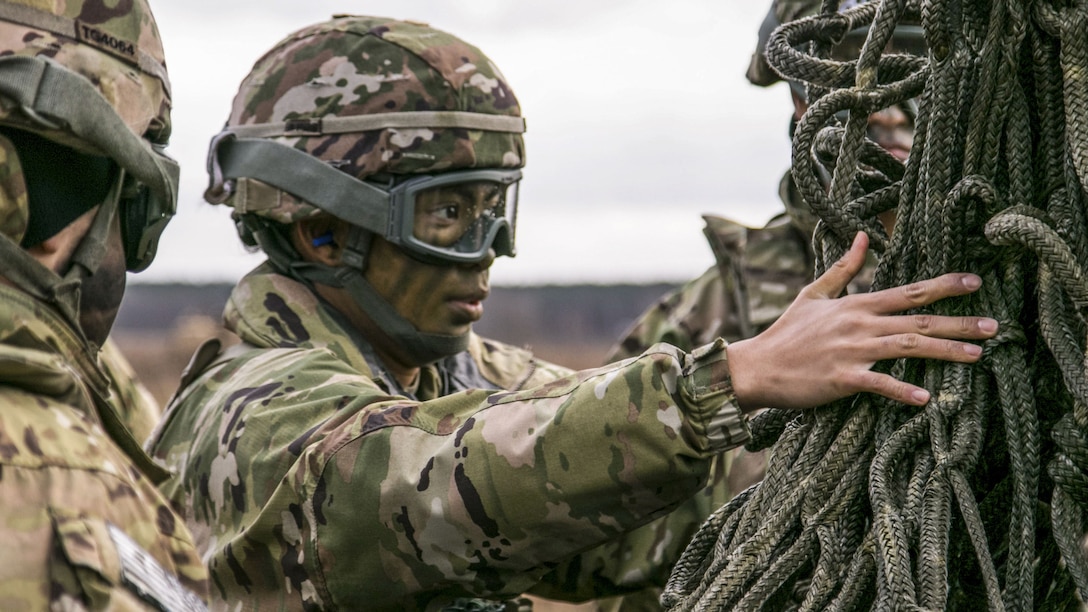 A soldier wearing a helmet and camouflage face paint handles netting.