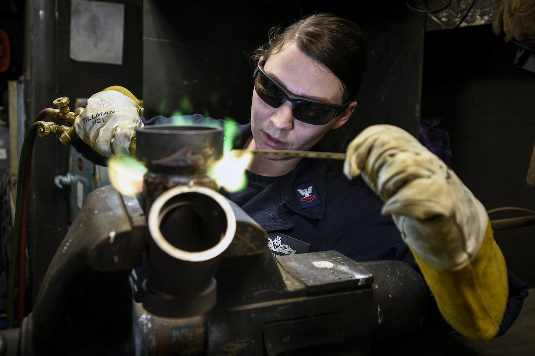 A sailor wearing protective gloves and eyewear brazes piping.