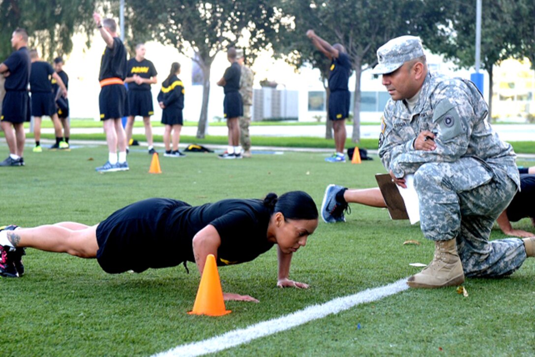 A woman does pushups while a military man watches.