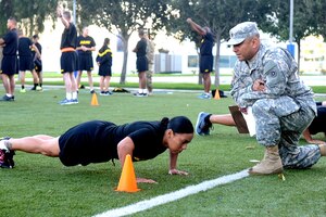 A woman does pushups while a military man watches.
