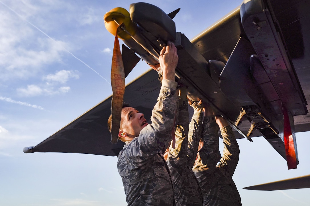 Two airmen load a missile onto the wing of an aircraft.