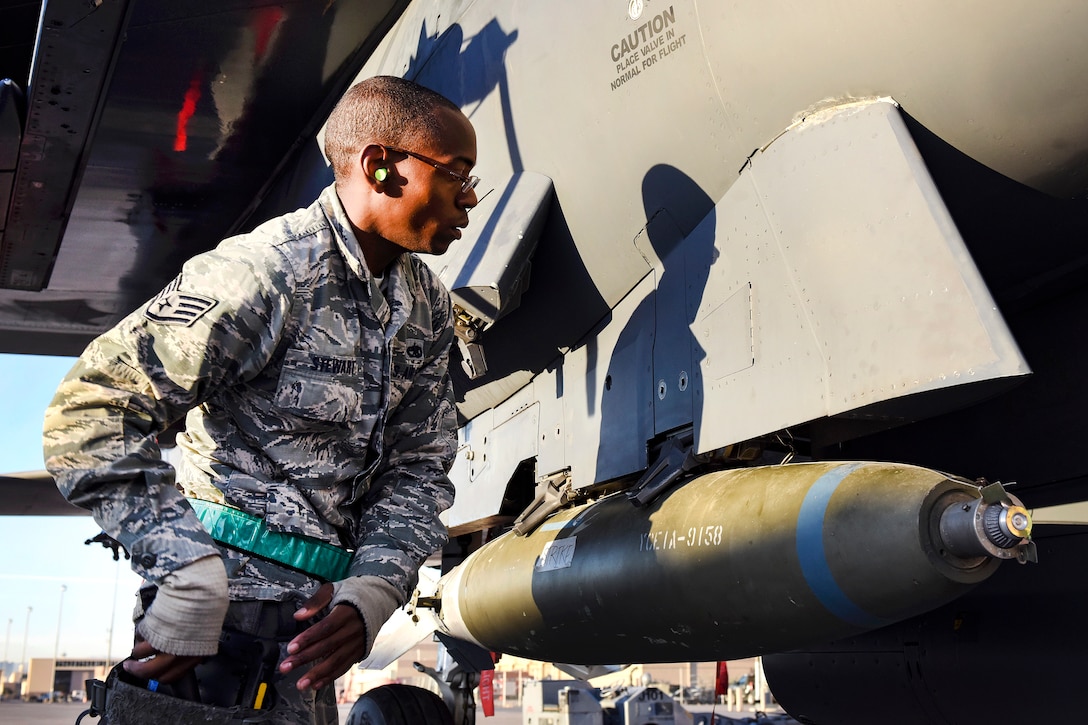 An airman looks at a bomb assembly on the side of an aircraft.