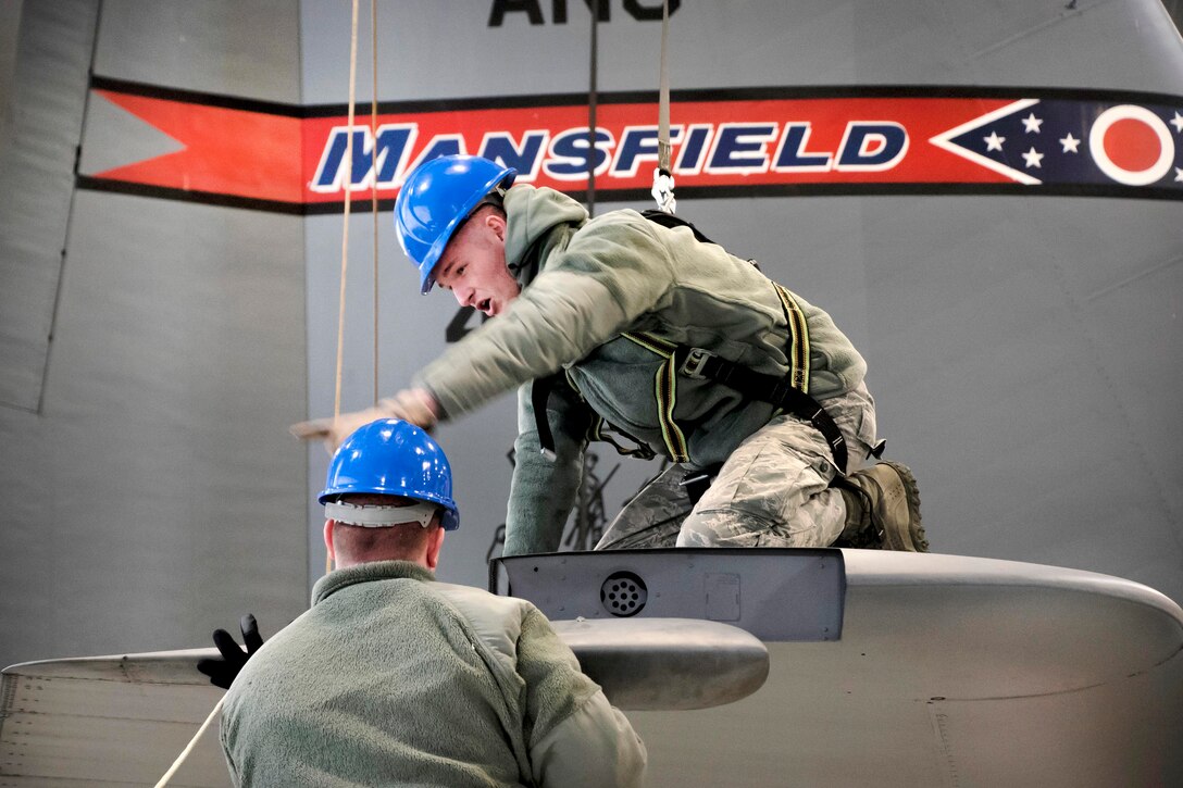 Two airmen work on the tail of an aircraft.