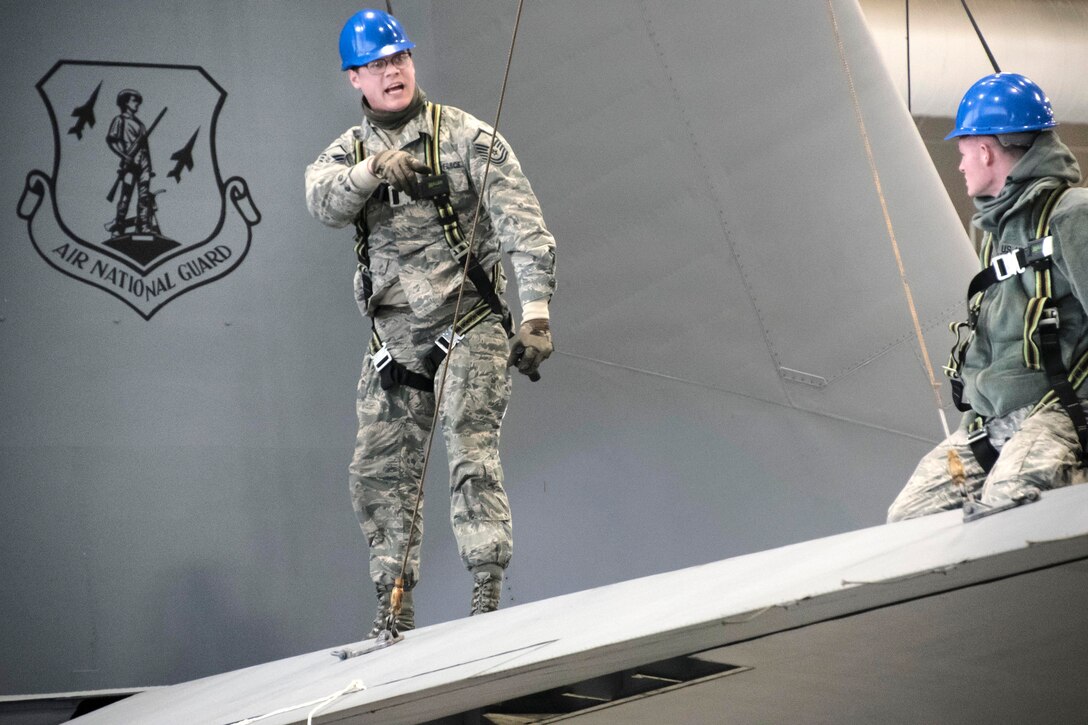 Two airmen work on the tail of an aircraft.
