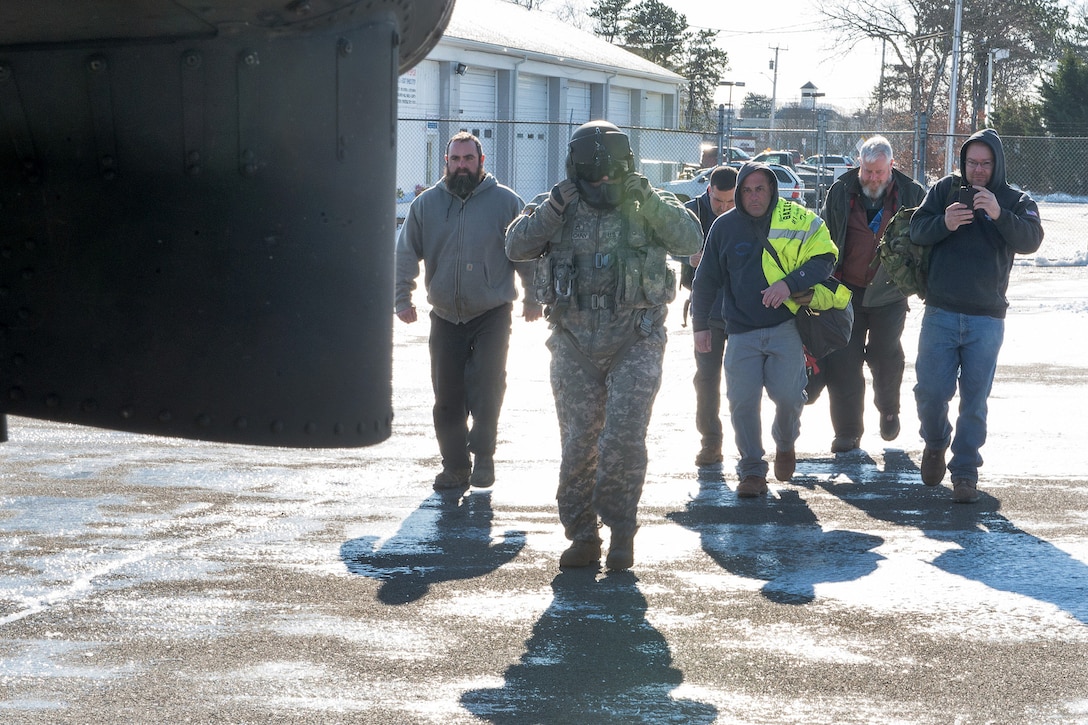 A National Guardsman leads five civilian contractors toward a helicopter.