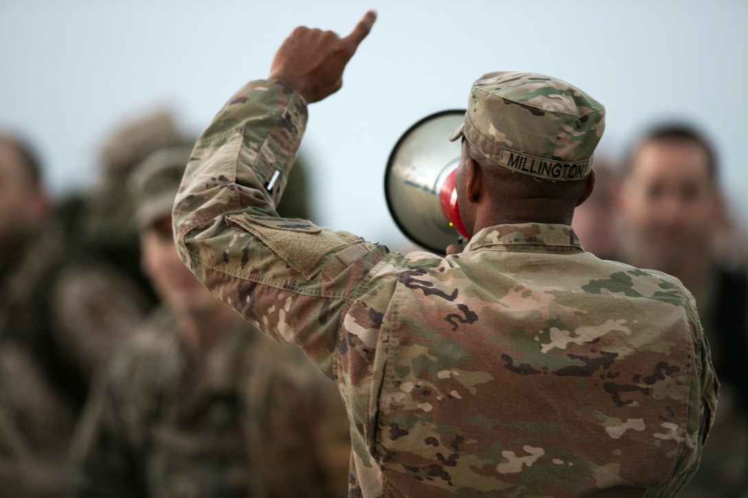 A soldier speaks to a group of soldiers using a megaphone.