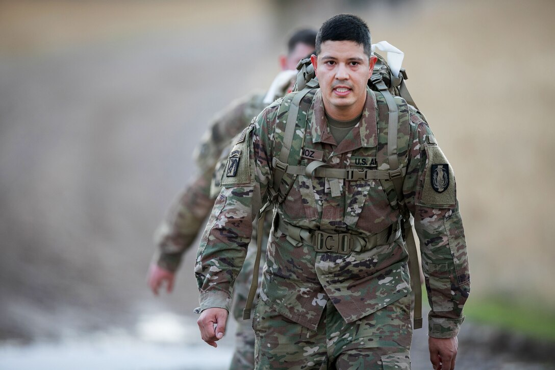 A soldier looks forward as he marches with a pack.
