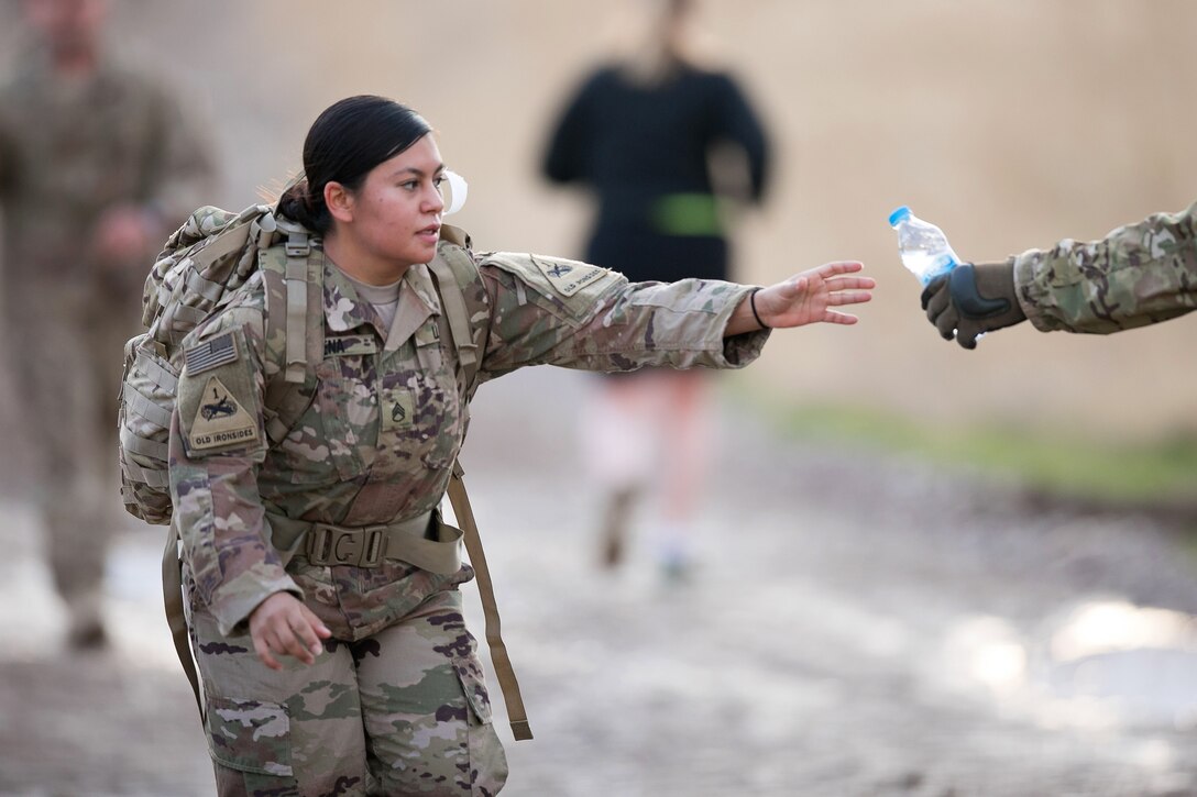 A soldier reaches for a bottle of watch while marching.