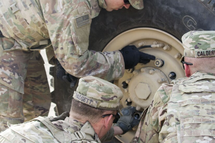 Three Soldiers changing a tire.