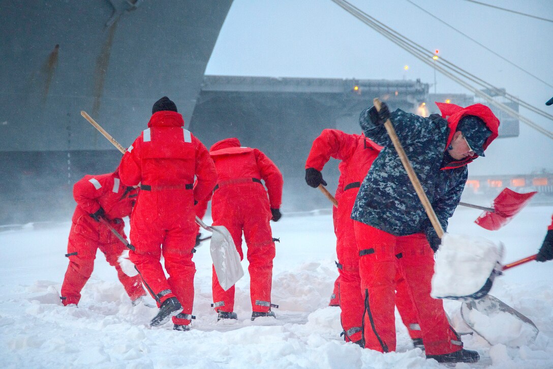 Sailors shovel snow off a pier near a ship.