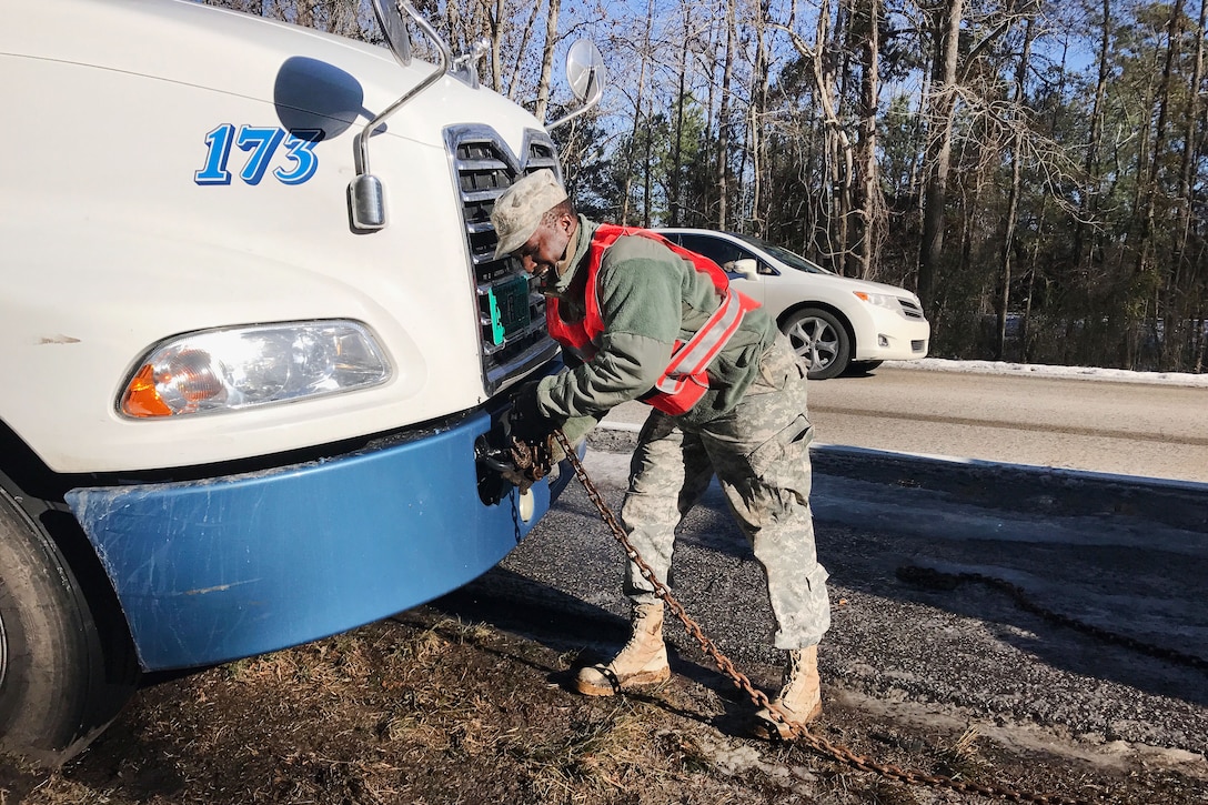 A guardsman attaches a chain to the front of an 18-wheeler.