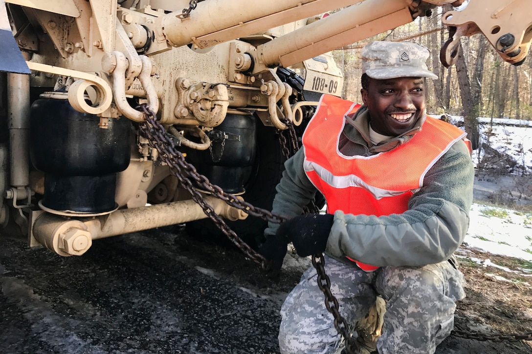 A soldier attaches a chain to a vehicle.