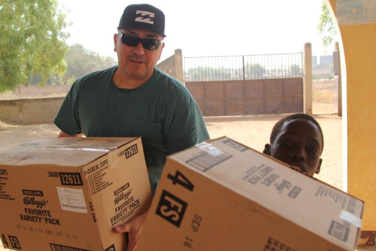 Army Sgt. Adrian Cordova, a mail clerk, carries food donated by American soldiers and civilians at the Saare Jabbama youth rehabilitation center in Garoua, Cameroon, Dec. 23, 2017. Army photo by Staff Sgt. Christina Turnipseed