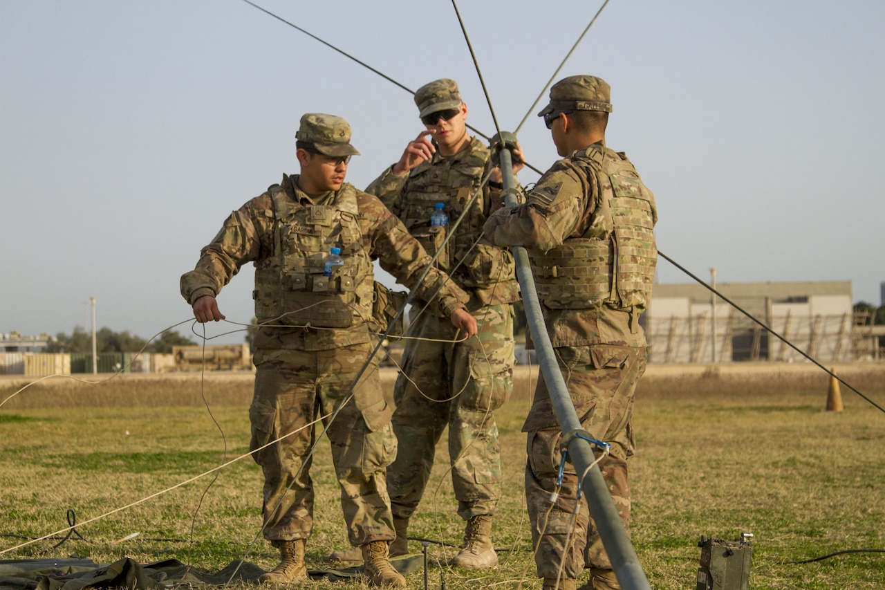 Three Soldiers setting up a radio communications antenna.