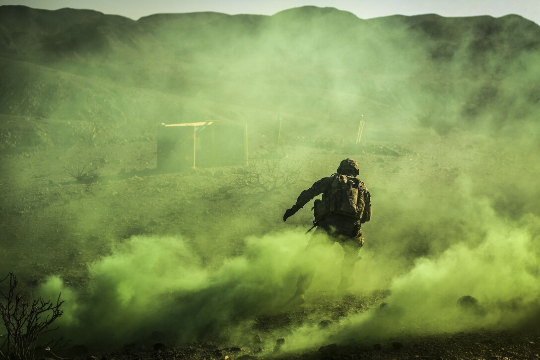 A soldier, shown from behind, runs as yellowish-green smoke billows around him.