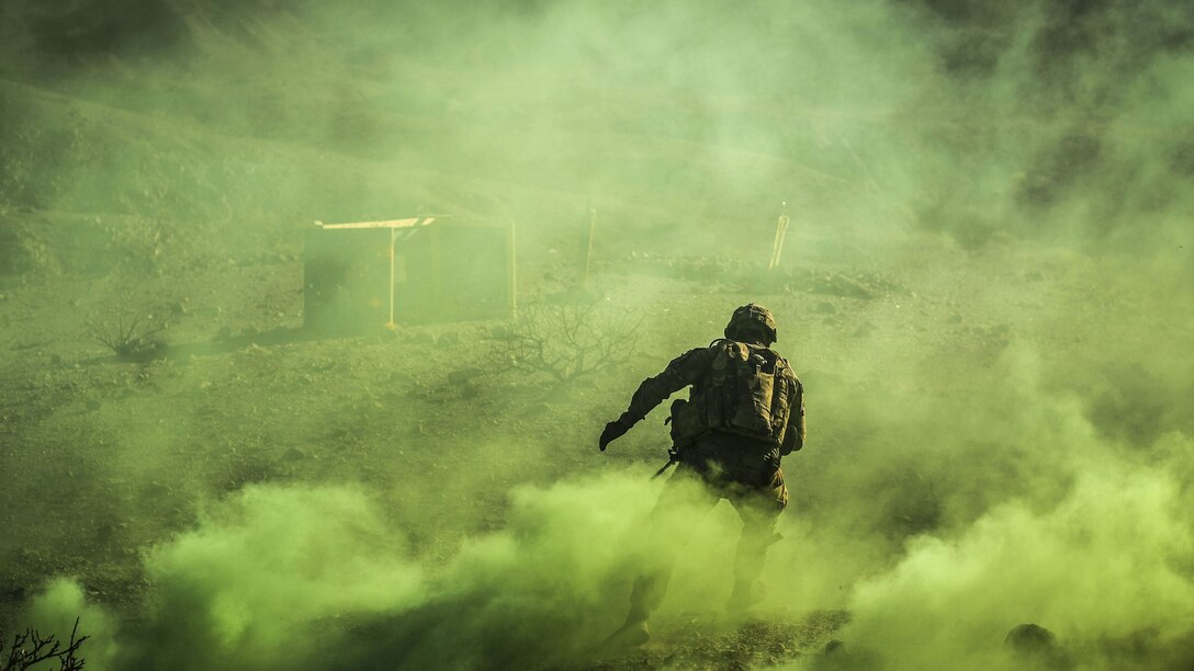 A soldier, shown from behind, runs as yellowish-green smoke billows around him.