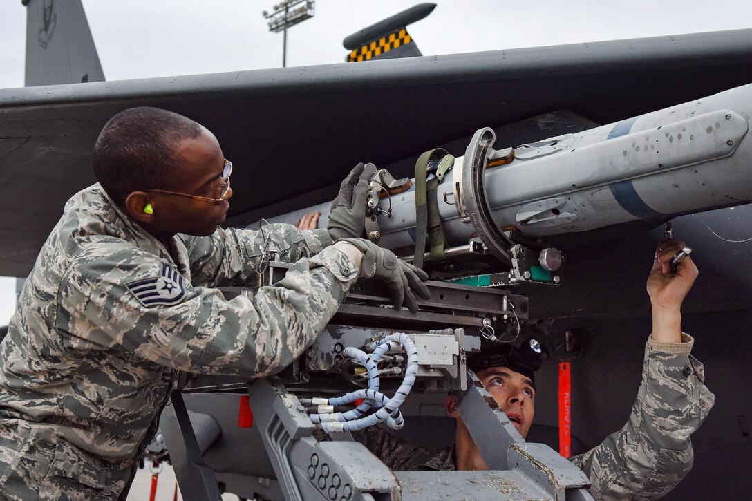 Staff Sgts. Mekai Stewart, left, and Brett Rosales-Carr load an AIM-120 missile onto an F-15 Eagle fighter aircraft.