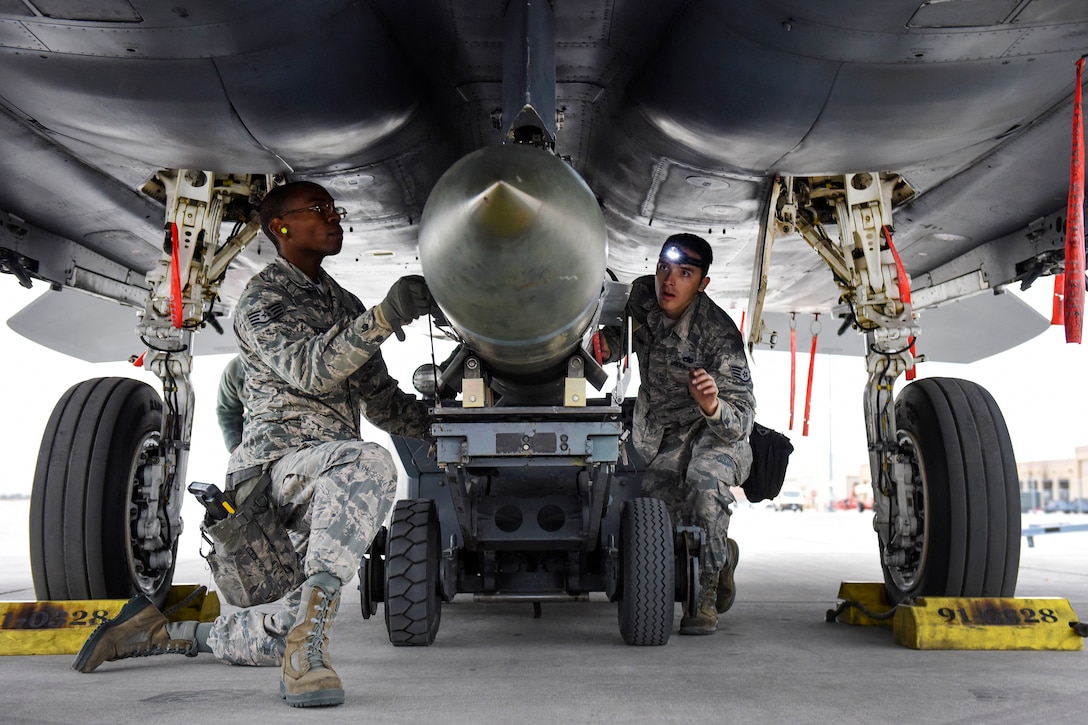 Airmen load a Mark 84 bomb on an F-15 Eagle fighter aircraft.