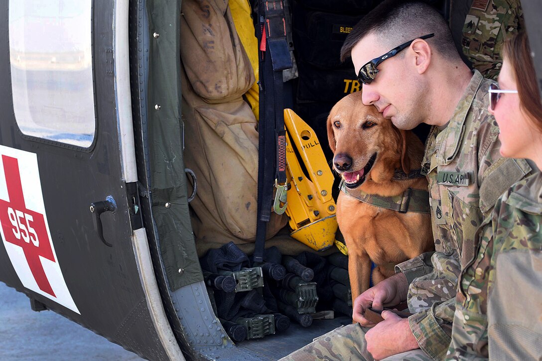 Army National Guardsmen and a military working dog sit inside a UH-60 Black Hawk medevac helicopter.