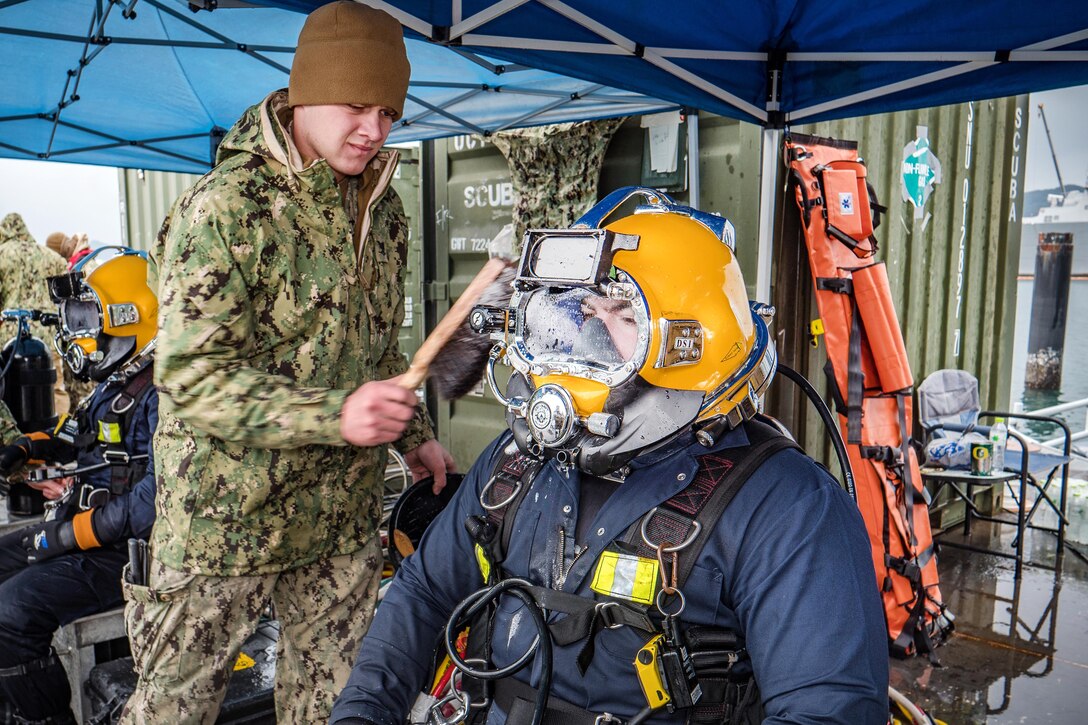 Navy Petty Officer 3rd Class Lucas Jackson checks for helmet leaks on Navy Petty Officer 1st Class Matthew Ramirez.