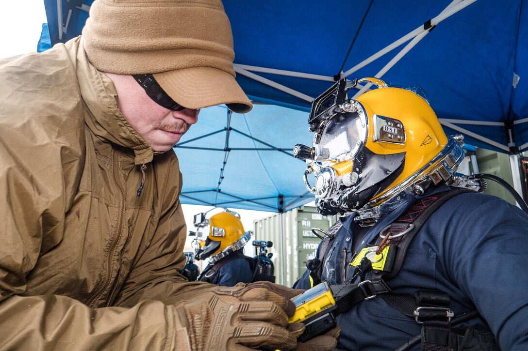 Navy Petty Officer 2nd Class Tim Dailey, left, performs dive supervisor checks on Navy Petty Officer 1st Class Matthew Ramirez.