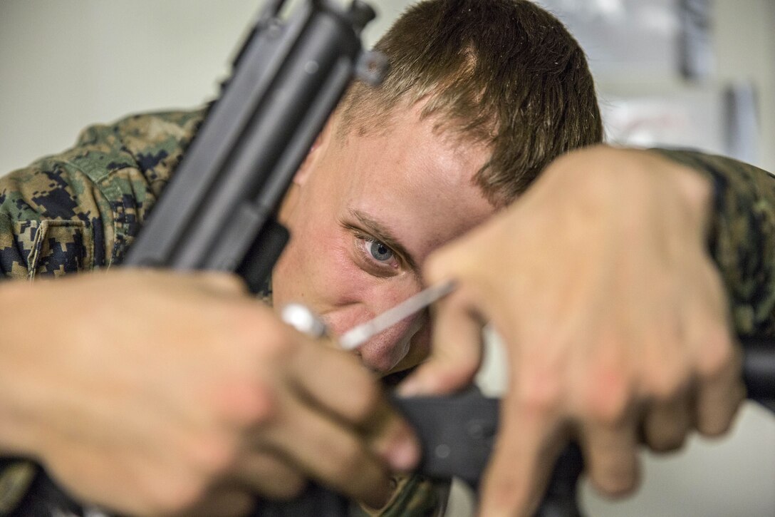 A Marine uses both hands to remove a rifle hammer while staring intently at it.