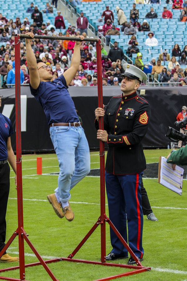 Staff Sergeant Bruno Bego, canvassing recruiter with Recruiting Substation Jacksonville, Recruiting Station Jacksonville, conducts a pull-up challenge during the TaxSlayer Bowl, Dec. 30, 2017, at EverBank Field in Jacksonville, Florida. Future Marines participated in a pull-up challenge to test their strength against other teams in front of the fans of Mississippi State University and the University of Louisville. (U.S. Marine Corps Photo by Sgt. Tony Simmons)