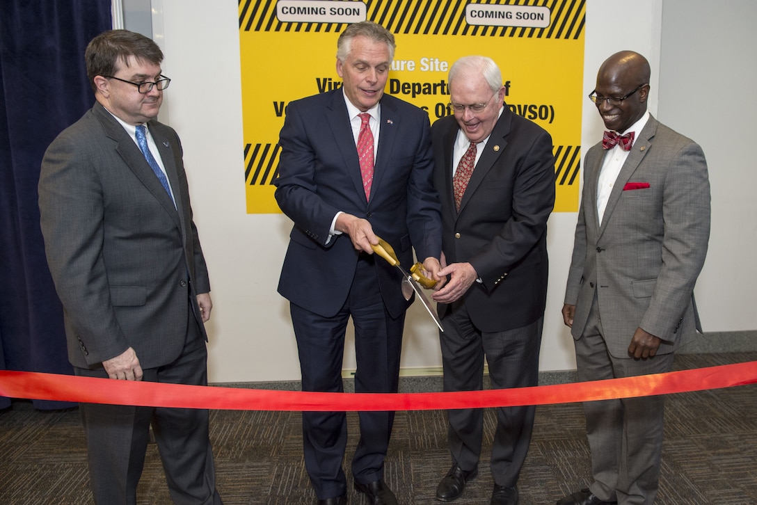 Two men prepare to cut a ribbon while two others watch.