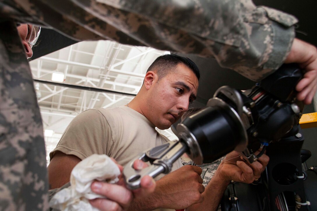 Spc. Pedro Nevarez installs a hoist device onto a UH-60 Black Hawk helicopter.