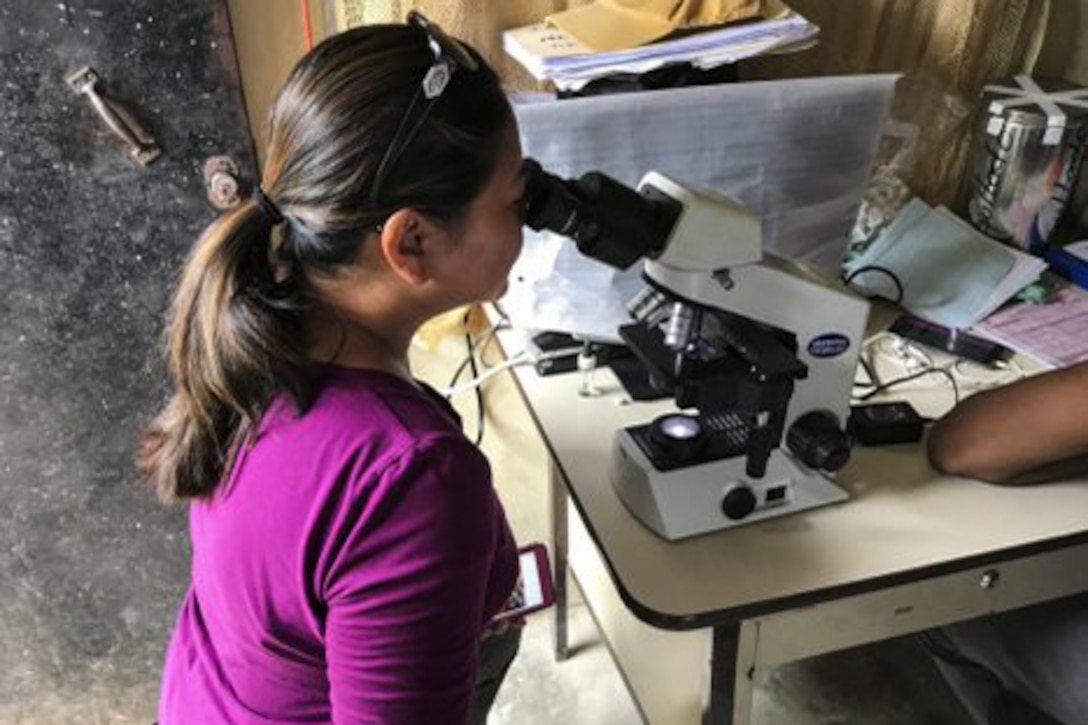 A woman looks through a microscope.