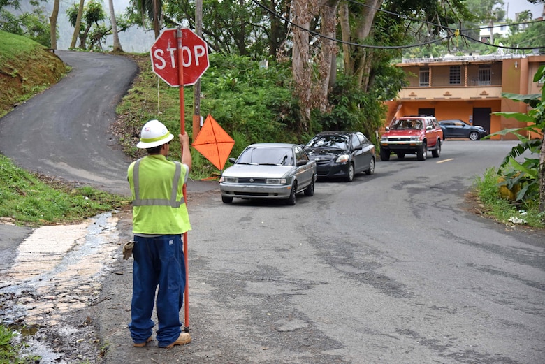 A flagman signals traffic to stop as the approach a crew from Fluor subcontractor MasTec working on a distribution line in Naranjito, Puerto Rico, Jan. 6, as part of Task Force Power Restoration's mission to repair the island's damaged electrical grid.