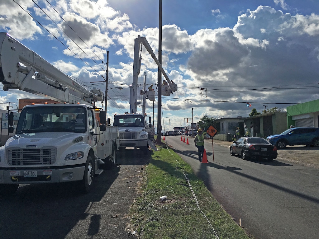 A flagman signals traffic to slow as they pass a crew of linemen from Fluor subcontractor MasTec working on a distribution line in San Juan, Puerto Rico, Dec. 12, 2017, as part of Task Force Power Restoration's mission to repair the island's damaged electrical grid.