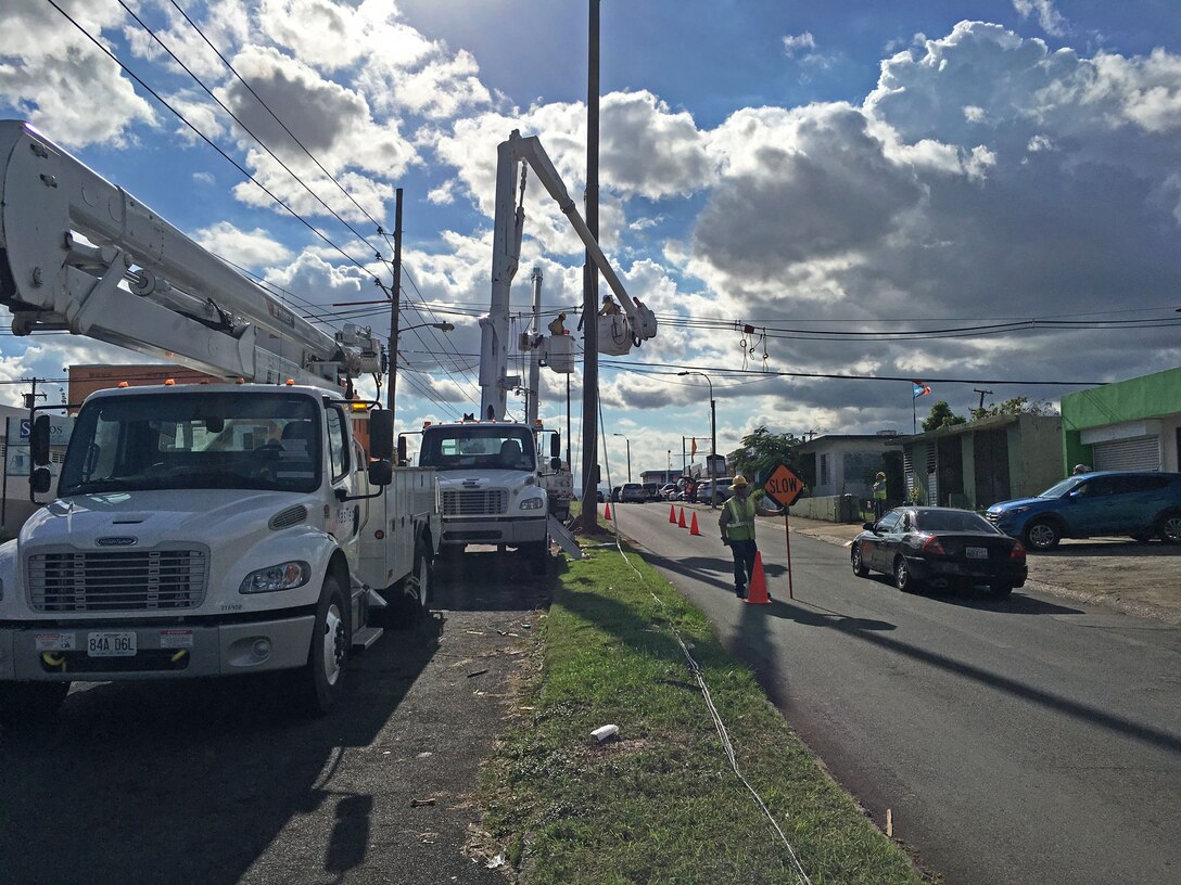 A flagman signals traffic to slow as they pass a crew of linemen from Fluor subcontractor MasTec working on a distribution line in San Juan, Puerto Rico, Dec. 12, 2017, as part of Task Force Power Restoration's mission to repair the island's damaged electrical grid.