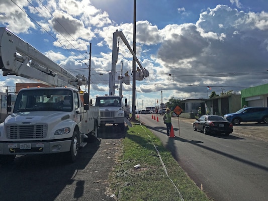 A flagman signals traffic to slow as they pass a crew of linemen from Fluor subcontractor MasTec working on a distribution line in San Juan, Puerto Rico, Dec. 12, 2017, as part of Task Force Power Restoration's mission to repair the island's damaged electrical grid.