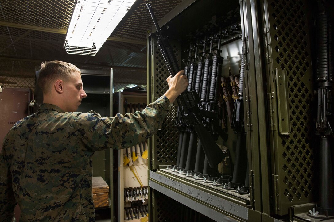 Marine Corps Lance Cpl. Jacob Cooper places a recently repaired M16A4 rifle on a rifle rack.