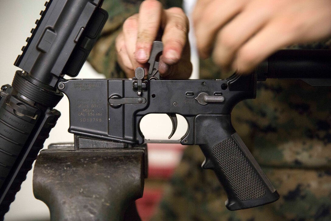 Marine Corps Lance Cpl. Jacob Cooper inserts a rifle hammer back into the lower receiver on an M16A4 rifle.