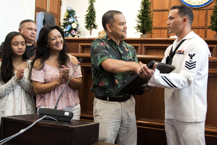 A sailor receives an award with people watching.