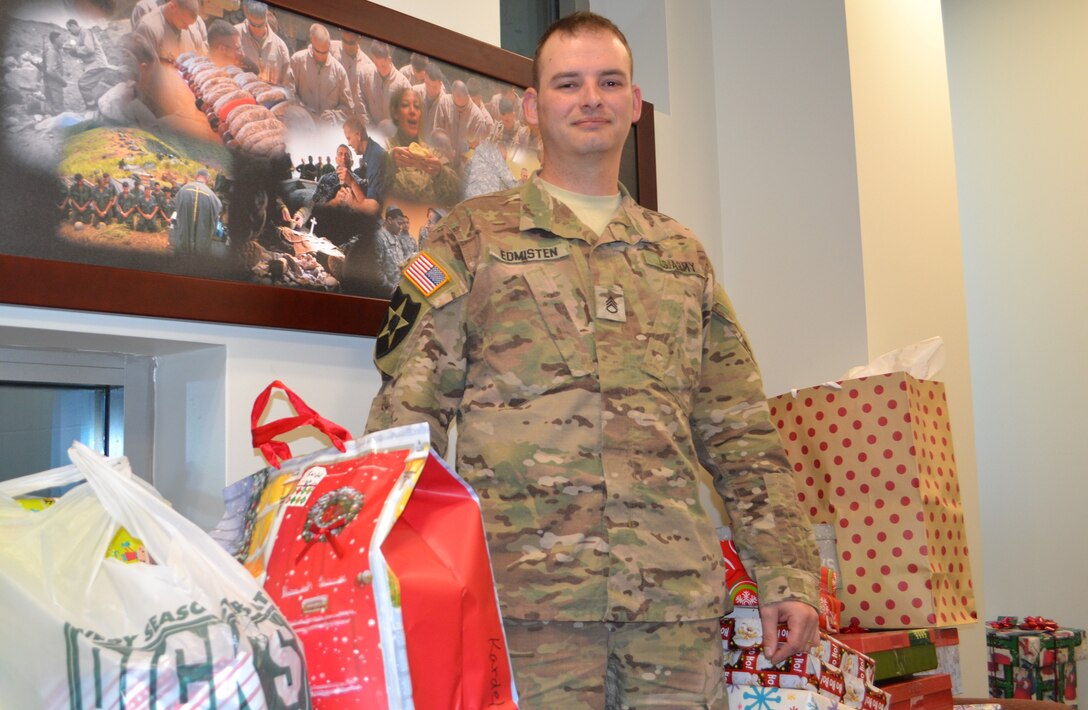 Staff sergeant in ACUs standing with gifts in office, facing viewer