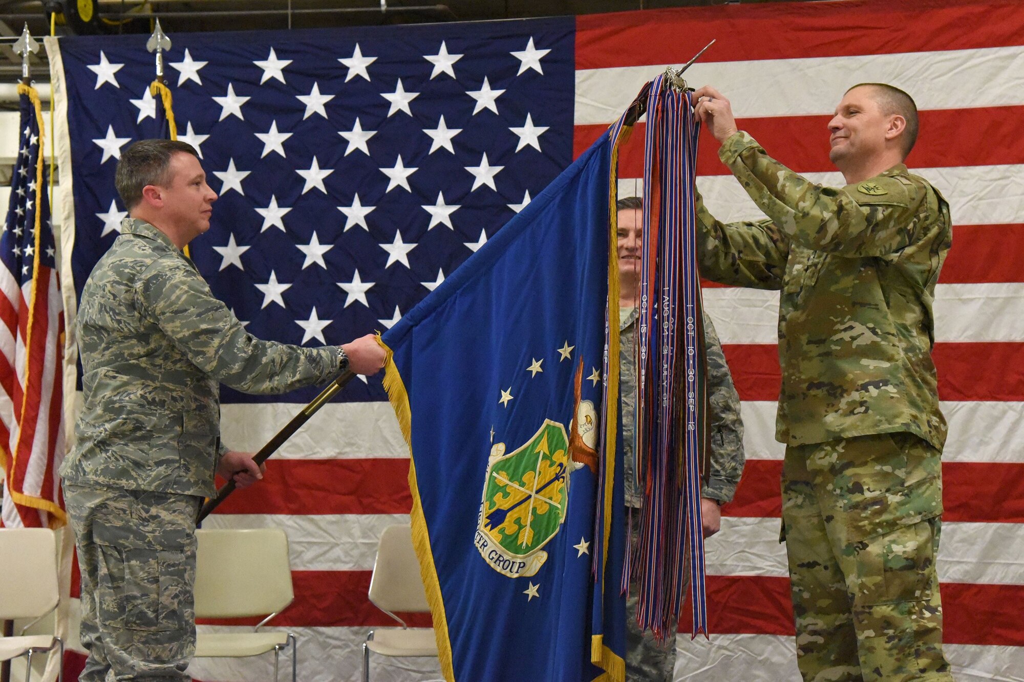 Maj. Gen. Al Dohrmann, the North Dakota adjutant general, right, attaches a streamer, representing the Air Force Outstanding Unit Award, onto the 119th Wing guidon, as Col. Britt Hatley, the 119th Wing commander, lowers the unit flag during a recognition ceremony as Chief Master Sgt. Duane Kangas, the 119th Wing command chief master sergeant, center, looks on at the North Dakota Air National Guard Base, Fargo, North Dakota, Jan. 6, 2018.
