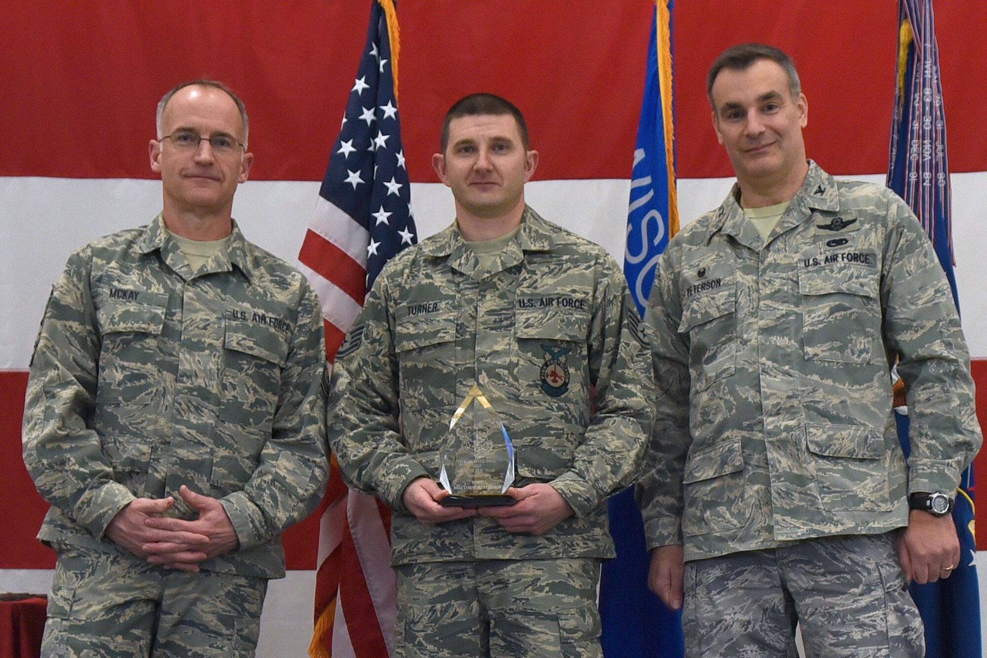 Command Chief Master Sgt. James McKay (left) joins 115th Fighter Wing Commander Col. Erik Peterson (right) to recognize fire protection journeyman Staff Sgt. Matthew Turner as noncommissioned officer of the year during the 115th FW annual awards ceremony at Truax Field in Madison, Wisconsin, Jan. 6, 2017. The ceremony highlighted Airman from throughout the unit who displayed exemplary skill and leadership in the performance of their duties both at home, and in deployed locations around the world. (U.S. Air National Guard photo by Tech. Sgt. Andrea Rhode)