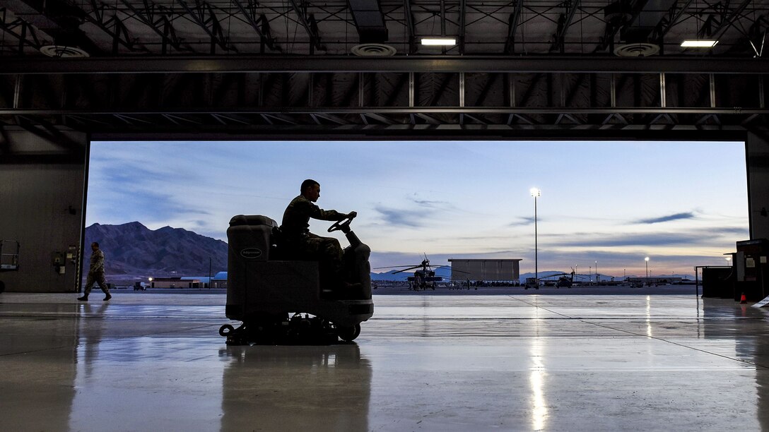 An airman, shown in silhouette, drives an auxiliary vehicle in a hangar.