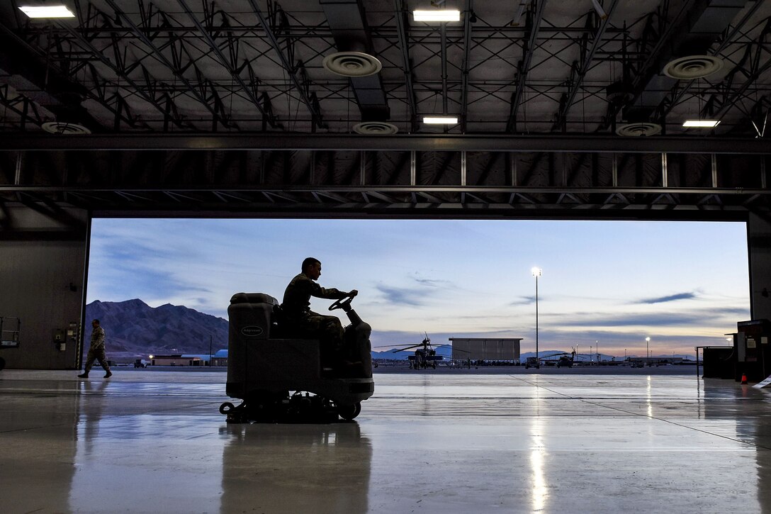 An airman, shown in silhouette, drives an auxiliary vehicle in a hangar.