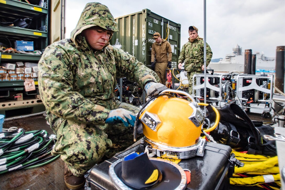 Petty Officer 1st Class Matthew Ramirez conducts predive maintenance on a KM-37 diving helmet.