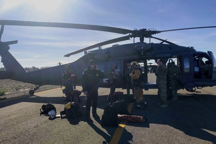 Six people stand outside of an HH-60G Pave Hawk rescue helicopter.