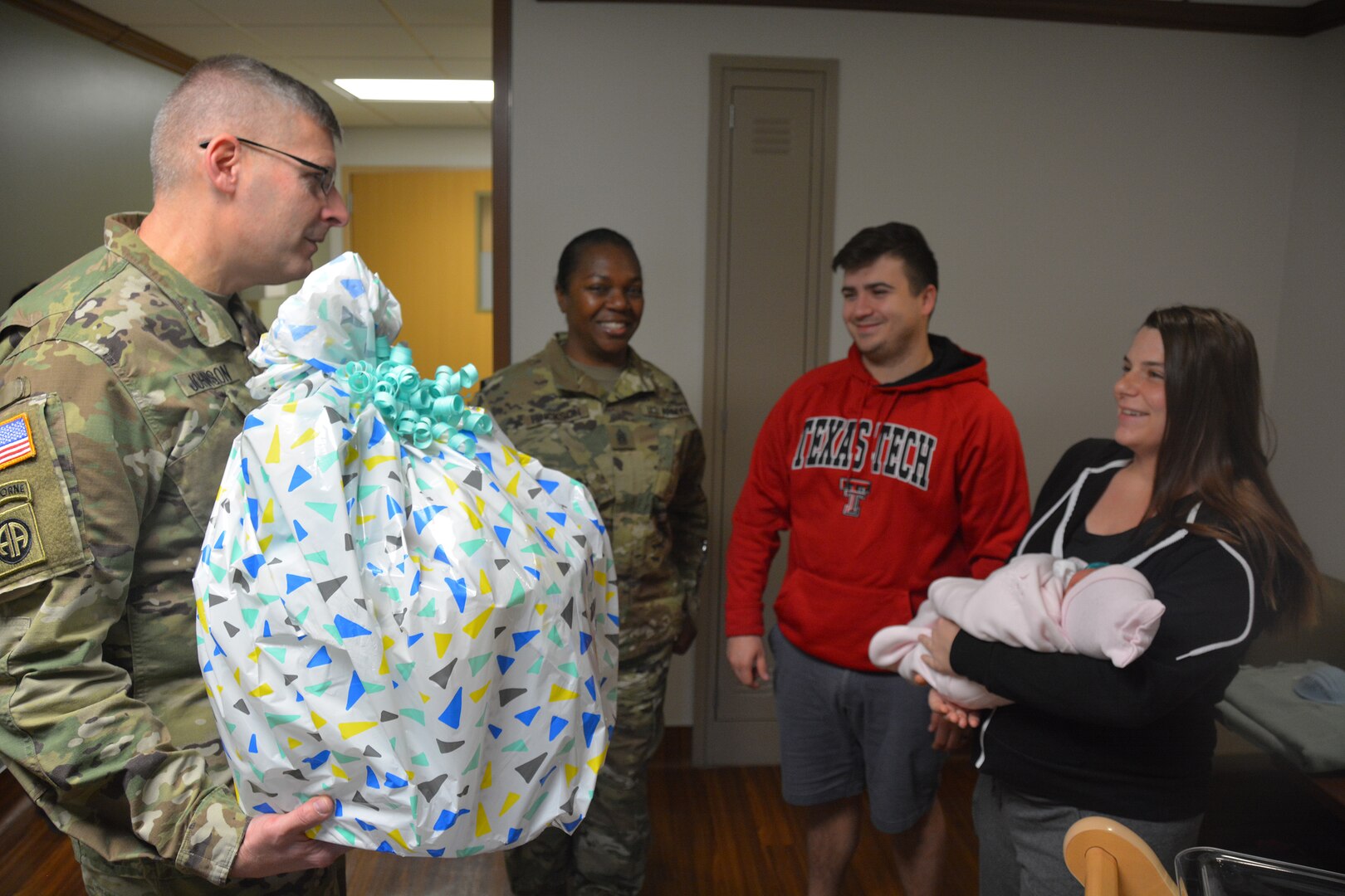 (From left) Brooke Army Medical Center commander Brig. Gen. Jeffrey Johnson and Warrior Transition Battalion Command Sgt. Maj. Karen Hinckson deliver a gift basket to Petty Officer 1st Class Dylan Pendleton, his wife, Rachel, and baby, Violet. Violet was BAMC's first baby in the New Year, born Jan. 1, 2018 at 2:27 a.m.