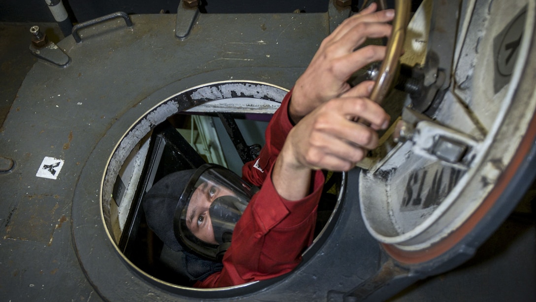 A sailor closes a scuttle during a drill on a ship.