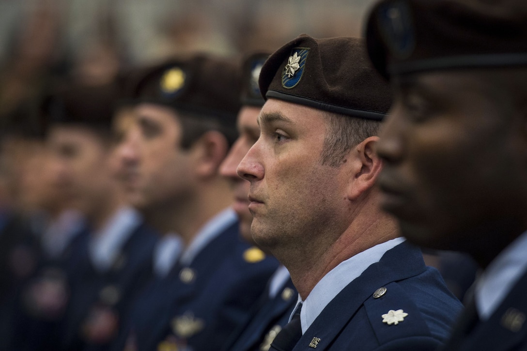 Airmen, shown in profile from the shoulders up, stand in a row wearing brown berets.