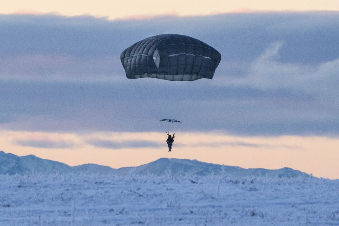 A soldier parachutes above a backdrop of snowy mountains and pale blue and pink sky.