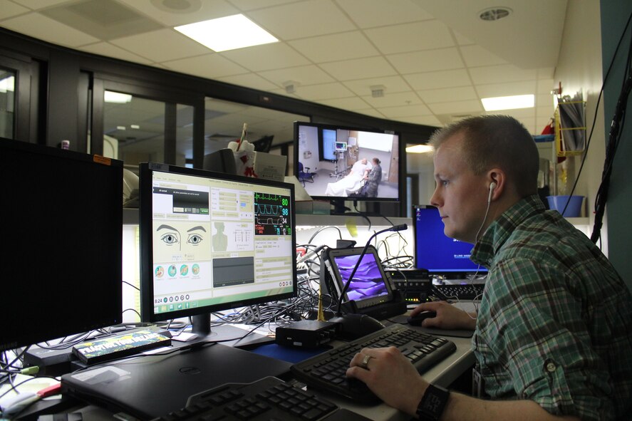 Johnny Cartwright, Certified Healthcare Simulation Operations Specialist, observes training from a monitor outside the training room. Cartwright can customize and control the actions of the mannequins to whatever training is required. (U.S. Air Force Photo/Stacey Geiger)