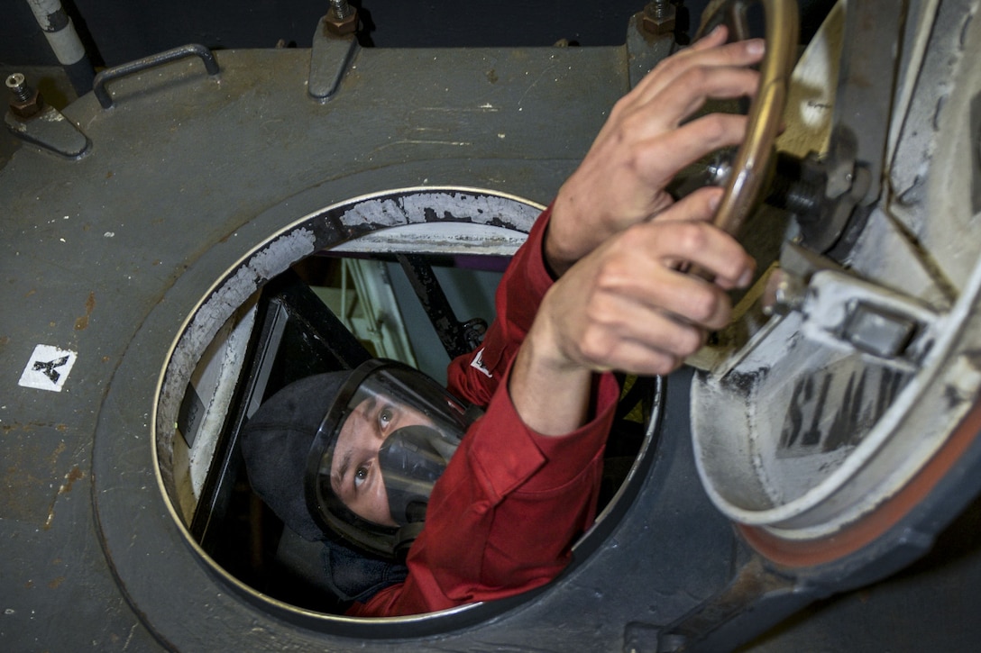 A sailor closes a scuttle during a drill on a ship.